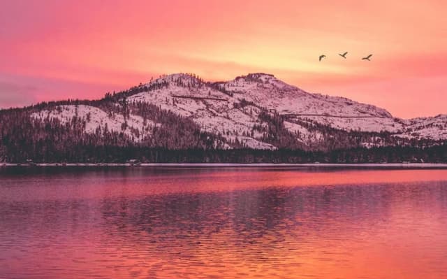 A pink and golden sunset view of snowy mountains overlooking a lake